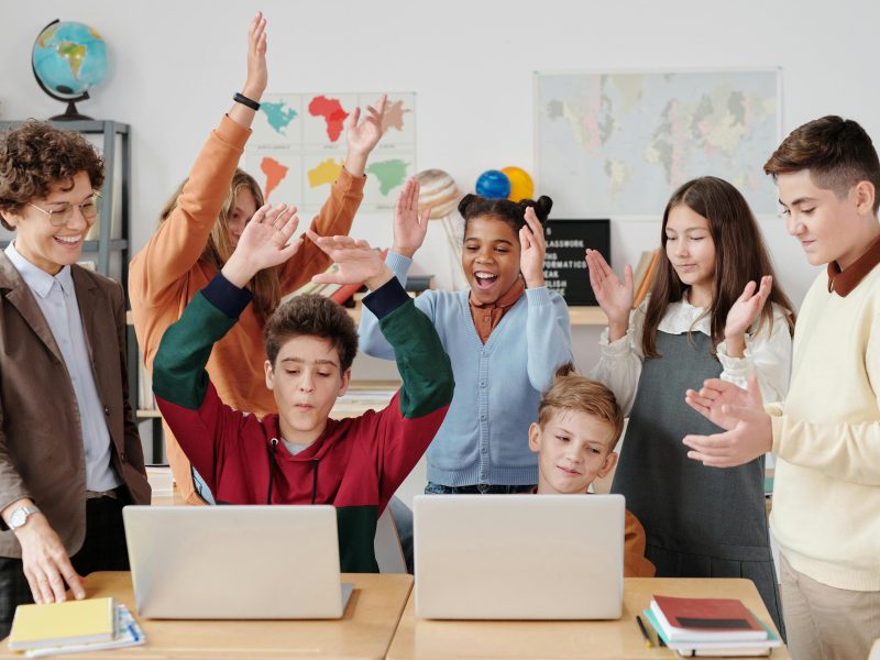 A group of happy students and a teacher clapping together in a school classroom.