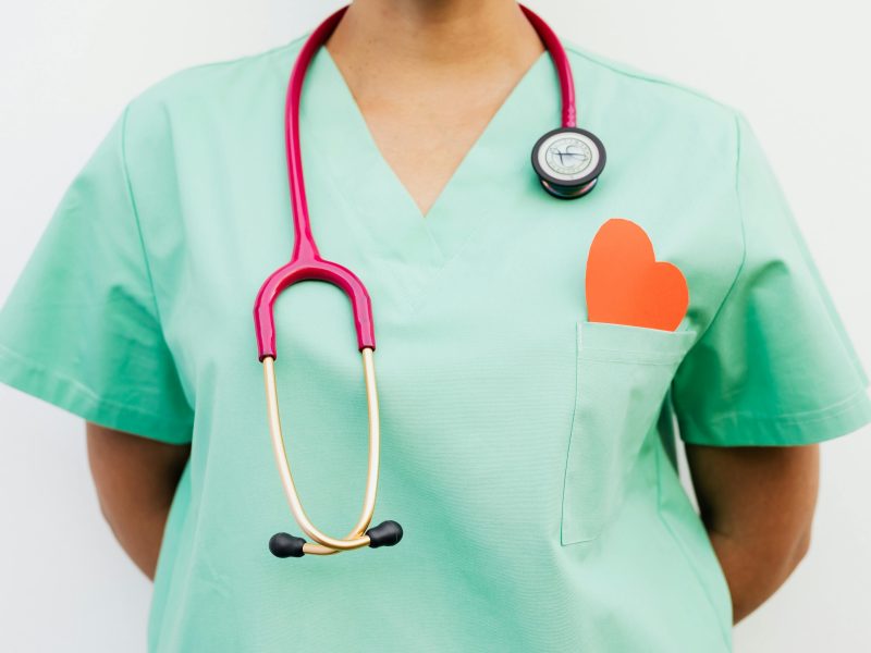 Close-up of a medical professional with a stethoscope and a paper heart cutout on a green uniform pocket.